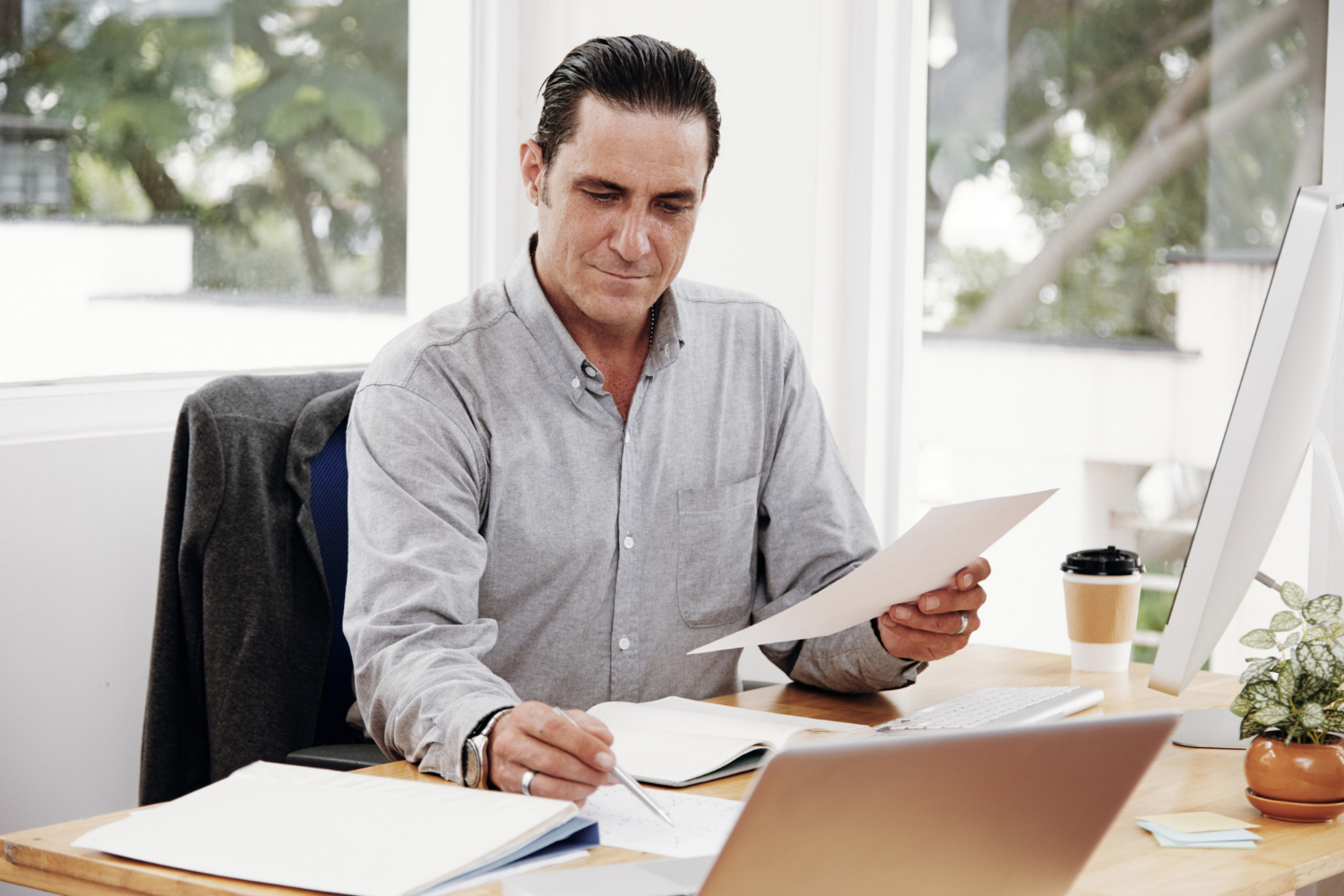 A man sitting at a desk in an office, reviewing documents and taking notes